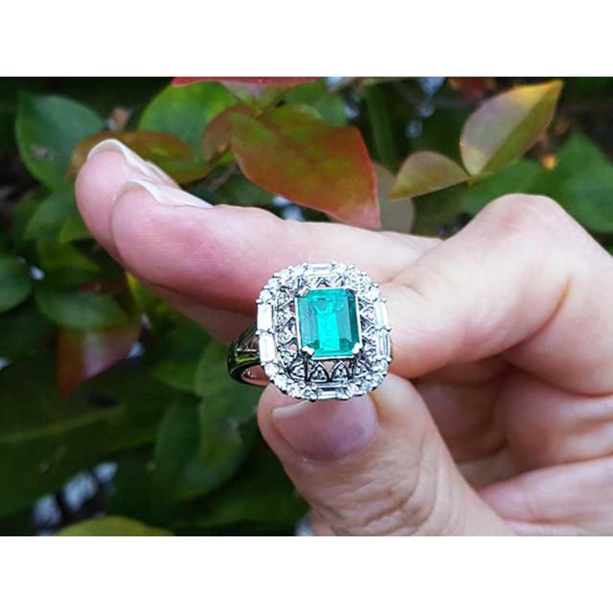 Vintage ring with a natural colombian emerald held between fingers against a blurred natural background.