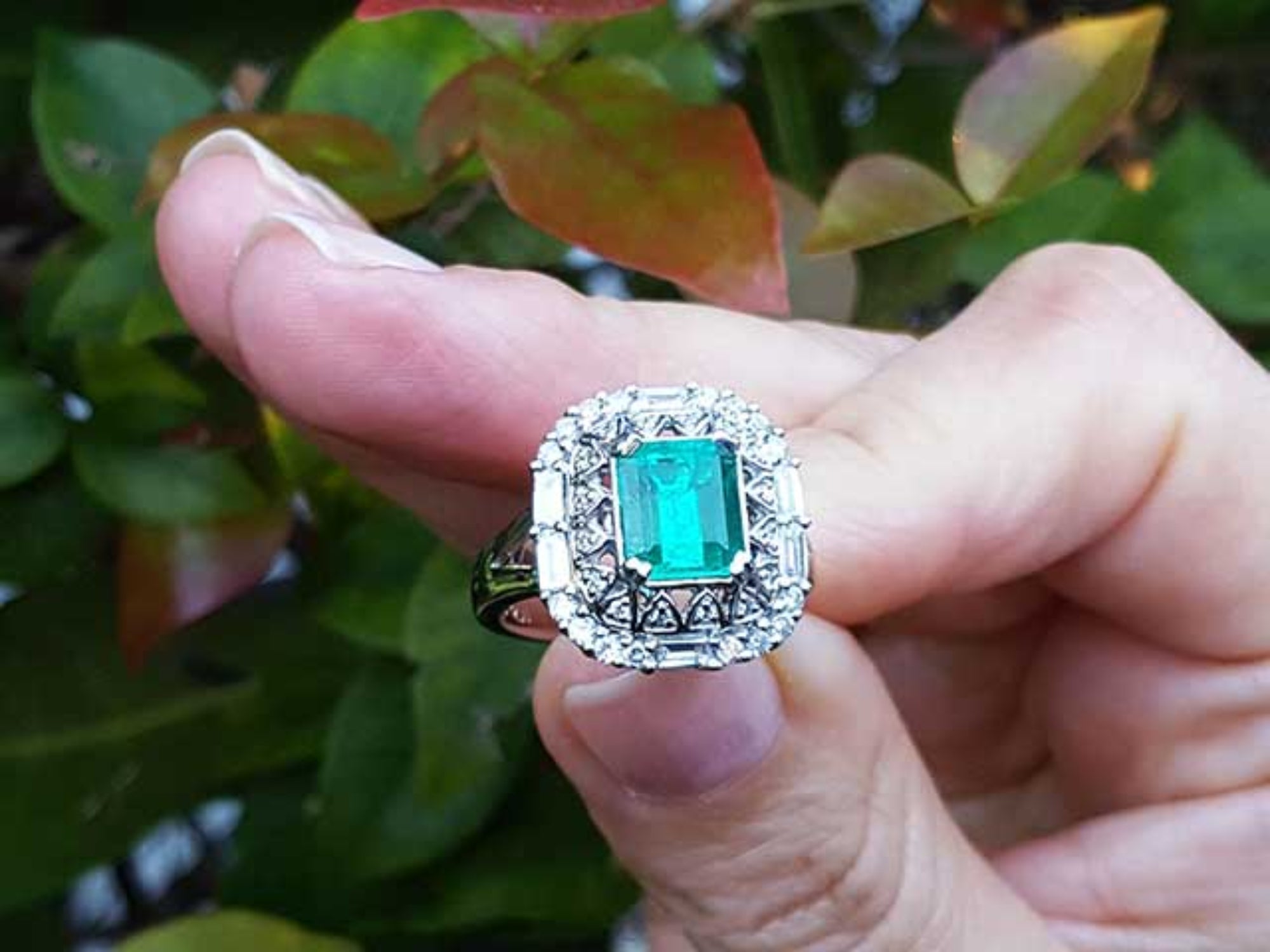 Vintage ring with a natural colombian emerald held between fingers against a blurred natural background.