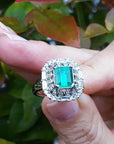 Vintage ring with a natural colombian emerald held between fingers against a blurred natural background.
