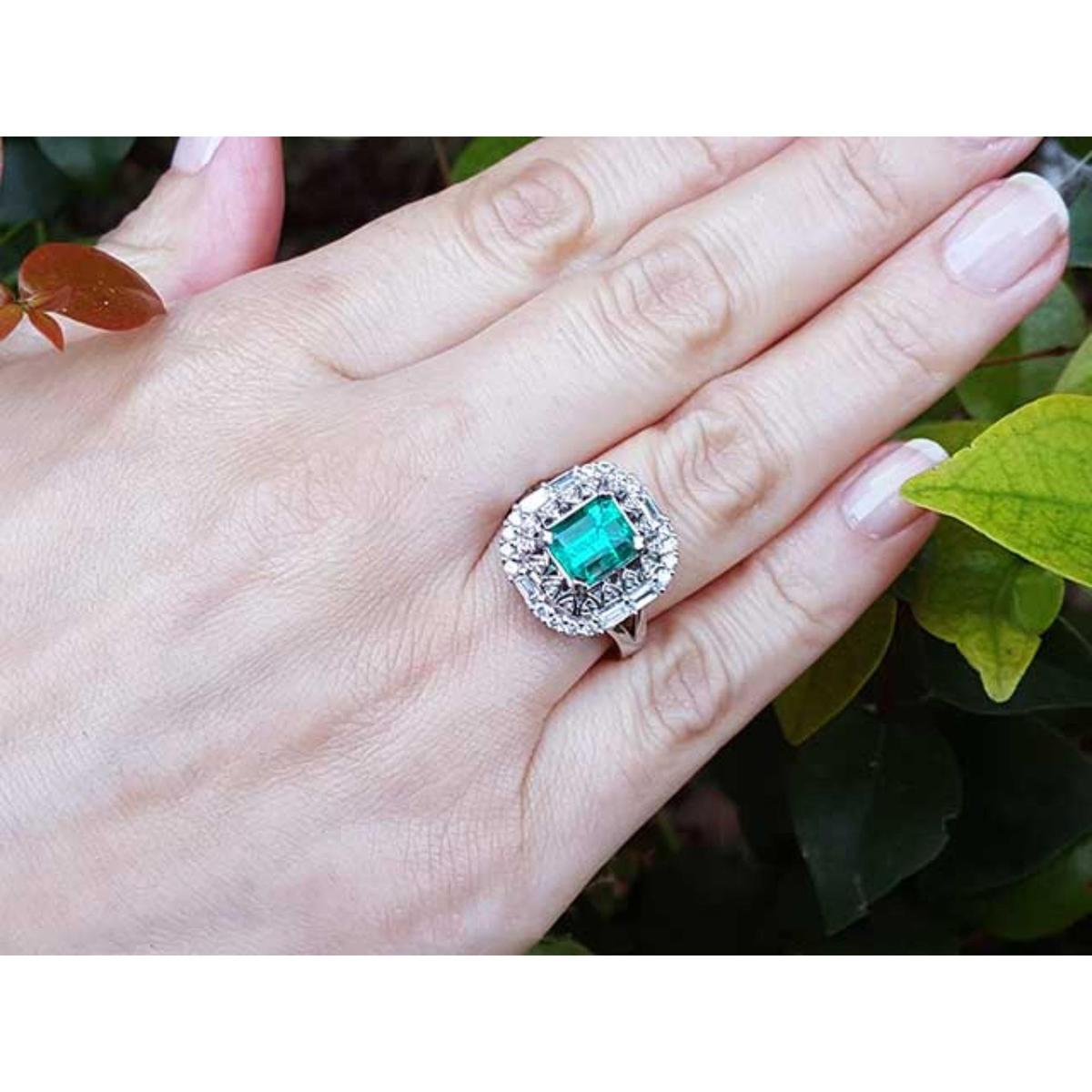 Hand wearing a vintage ring with a colombian emerald against a leafy background.