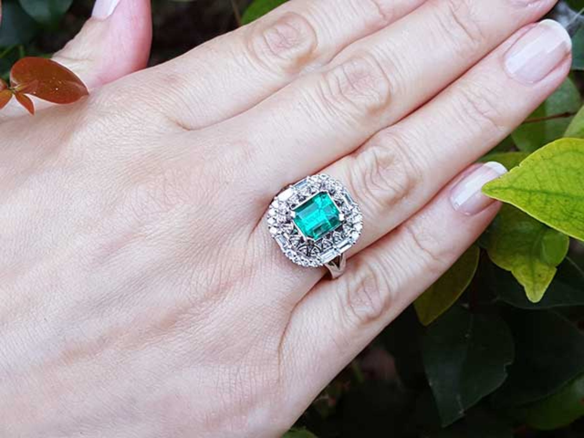Hand wearing a vintage ring with a colombian emerald against a leafy background.