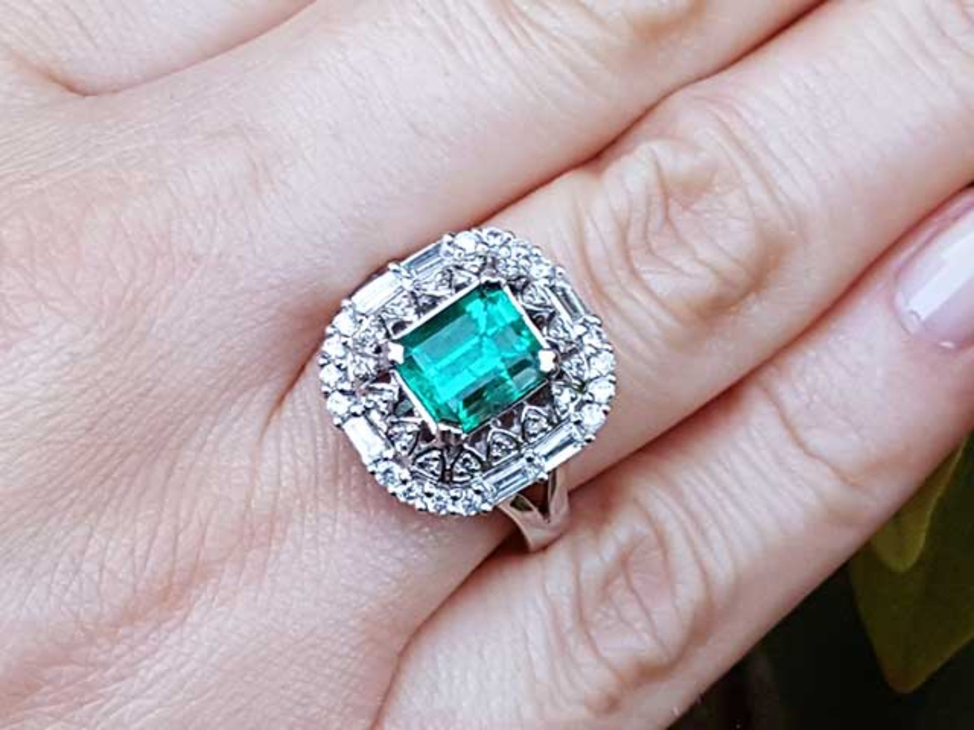 Ring with an emerald and diamond vintage ring on a hand.