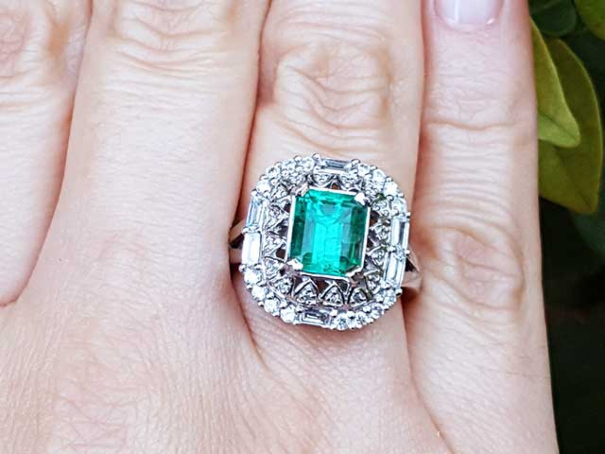 A vintage Colombian emerald ring with accent diamonds on a finger.