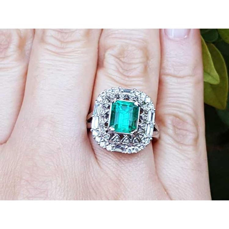 A vintage Colombian emerald ring with accent diamonds on a finger.