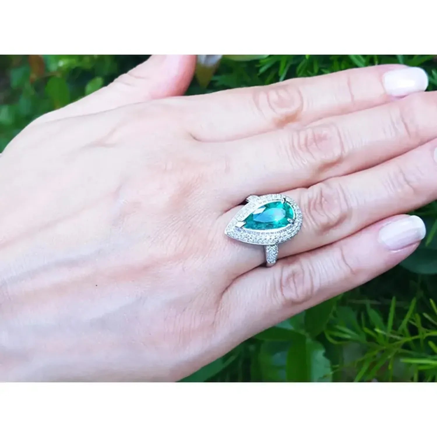 Anillo de oro blanco 14k con esmeralda colombiana corte pera de 3.35 ct rodeada de diamantes en mano.