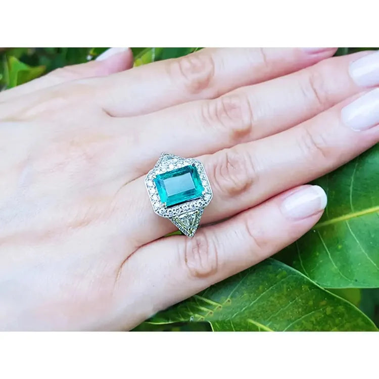 Vista mas cercana de mano de mujer vistiendo un anillo con esmeralda rodeada de diamantes.
