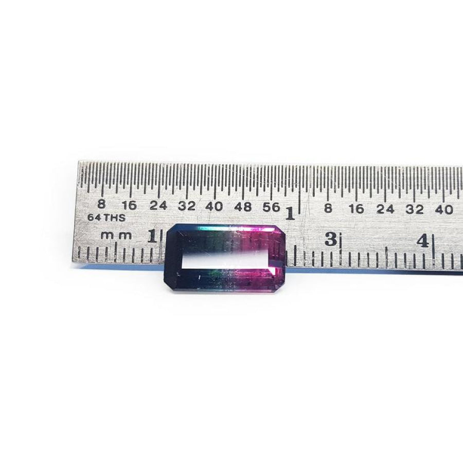 Rectangular emerald cut watermelon tourmaline with vibrant red-orange and deep blue-green colors, next to a ruler.