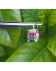 Multicolored tourmaline gemstone pendant held by tweezers against a green leaf background.