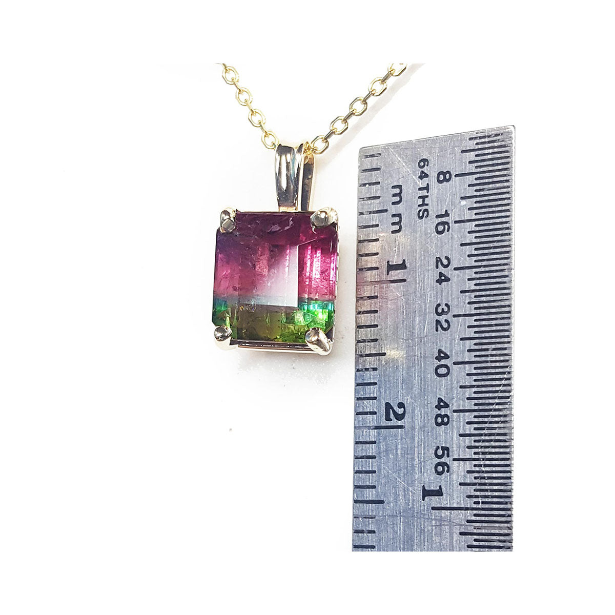 A natural watermelon tourmaline gemstone pendant on a chain with a ruler for scale on a white background