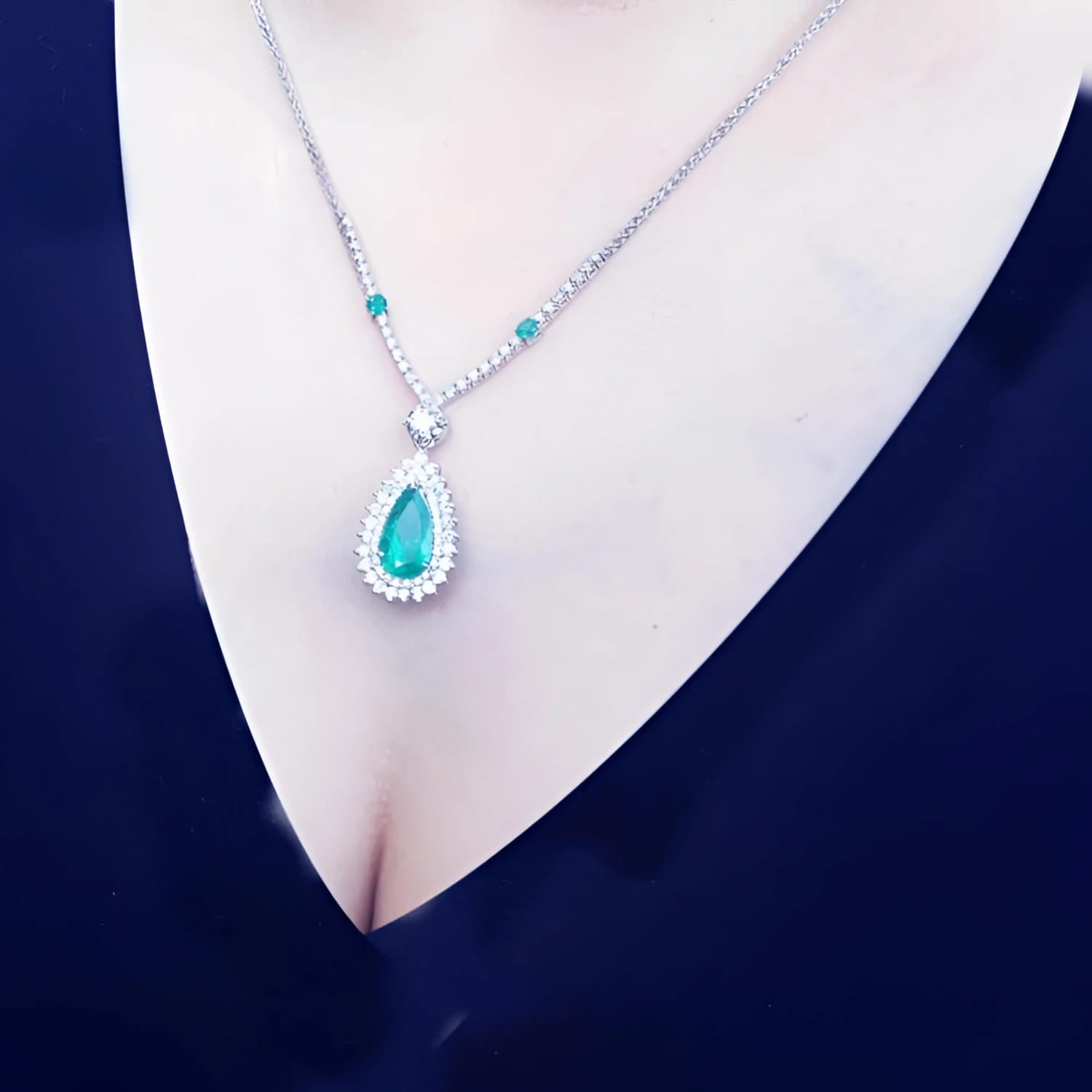 Pear cut emerald necklace with double diamond halo, 18K white gold chain, worn on a person.