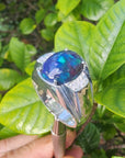 Sterling silver ring for men with a colorful black opal held against green leaves