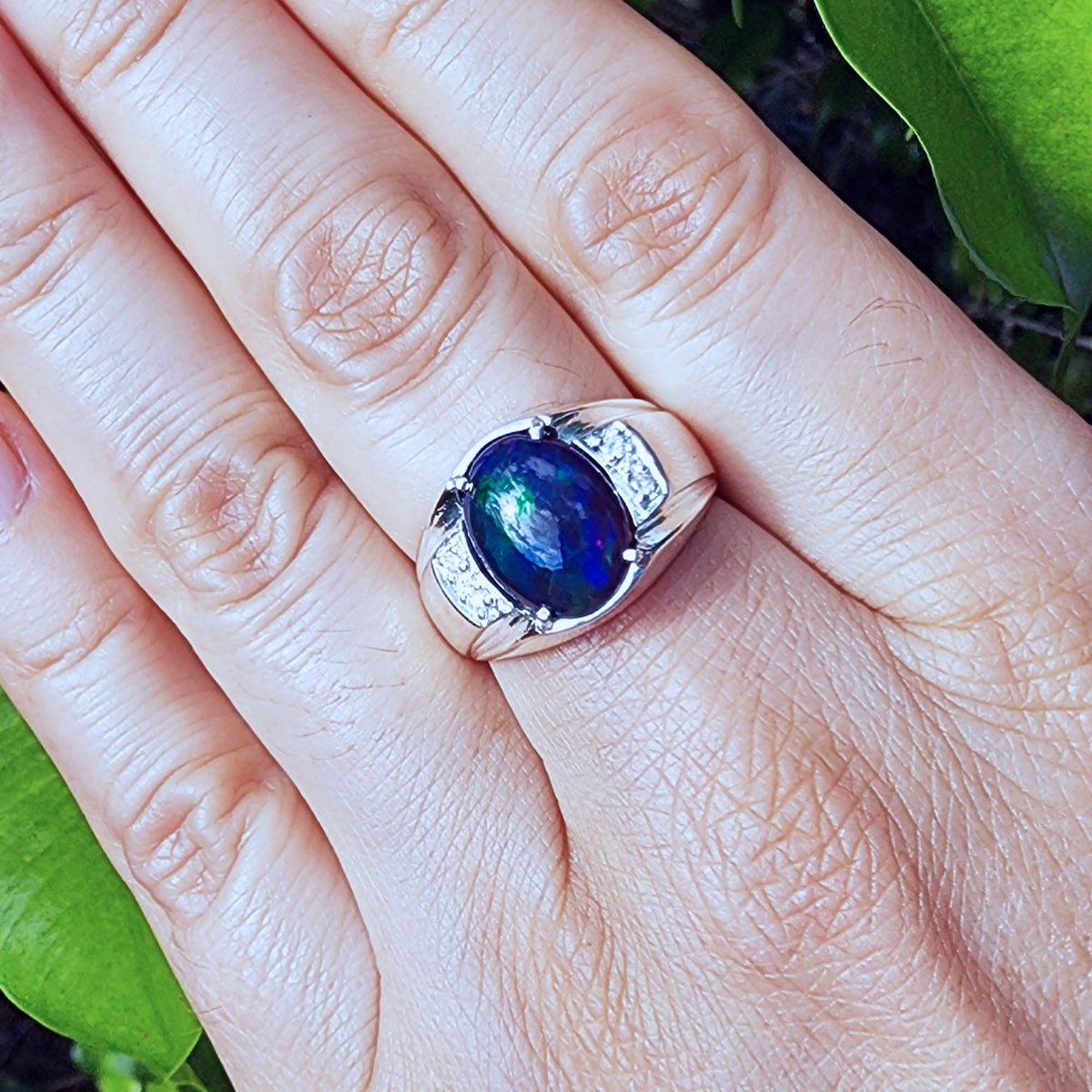 Ring with a blue Welo opal on a person's finger against a natural background