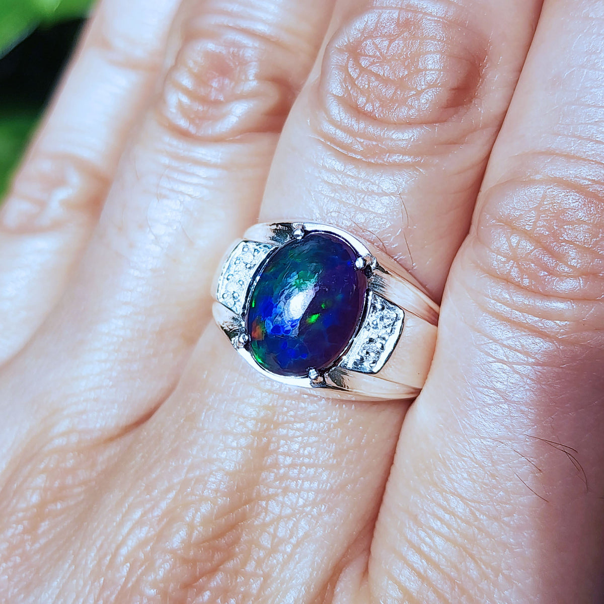 Silver ring with a colorful black opal on a person's finger