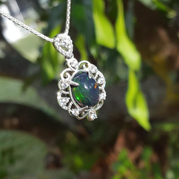Opal pendant with silver frame on a chain against a green leafy background
