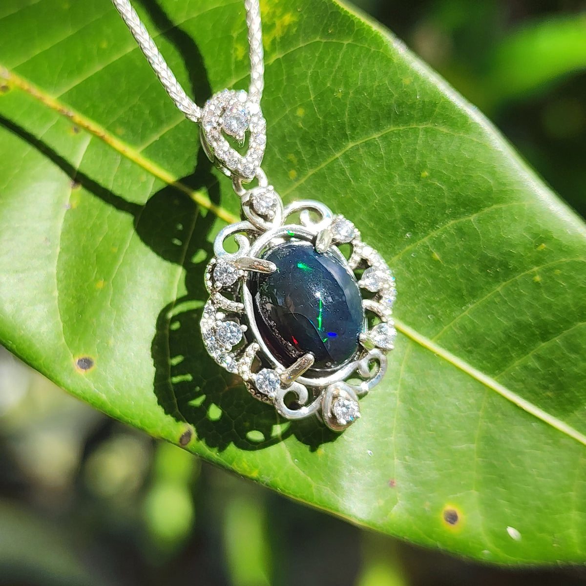 Opal pendant on a silver chain with green leaves in the background