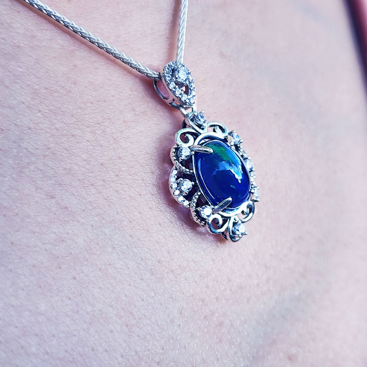 A multicolor Ethiopian black opal pendant on a chain against a skin background.