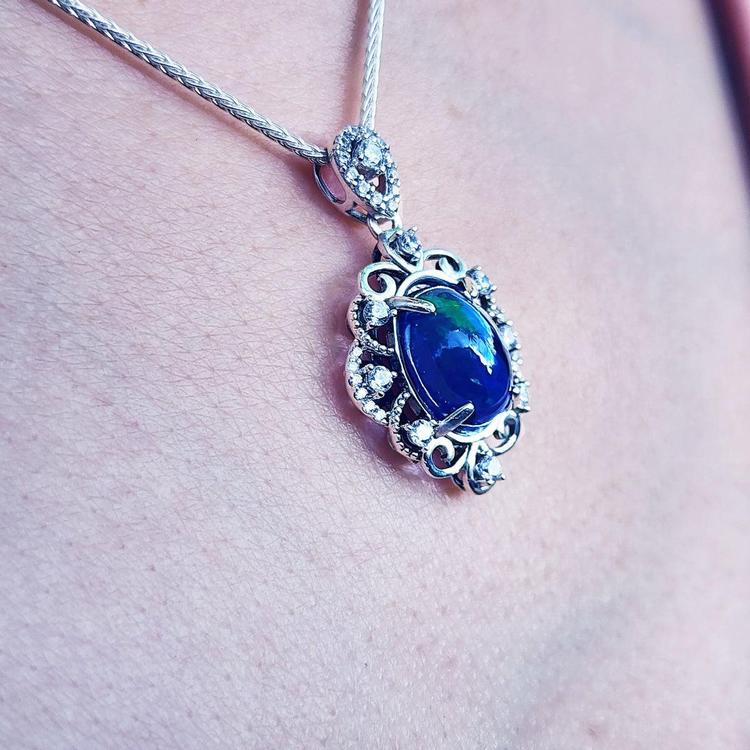 A multicolor Ethiopian black opal pendant on a chain against a skin background.