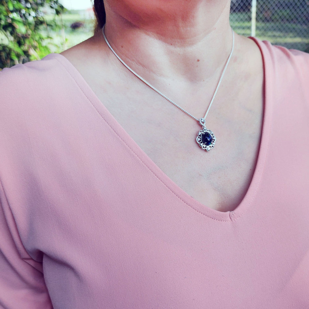 Person wearing a pink top with a silver necklace featuring a black opal pendant.
