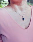 Person wearing a pink top with a silver necklace featuring a black opal pendant.