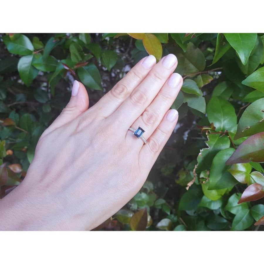 18K white gold ring with a radiant-cut blue sapphire and diamond accents on a woman's hand.