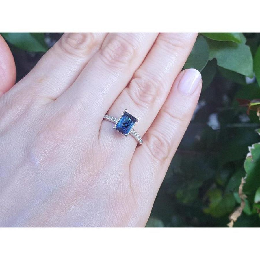 18K white gold ring with a radiant-cut blue sapphire and diamond accents on a woman's hand.