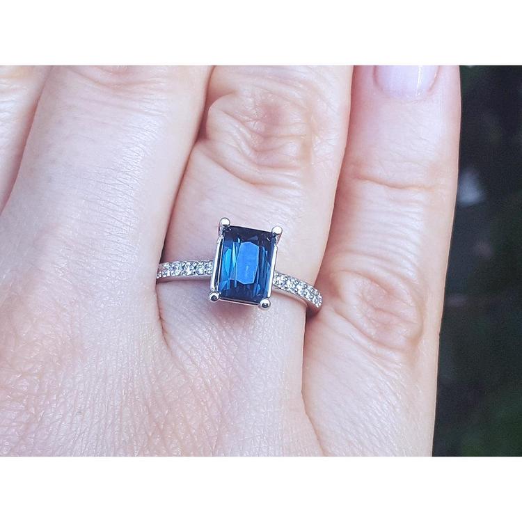 Blue sapphire ring white gold on a finger against a blurred background