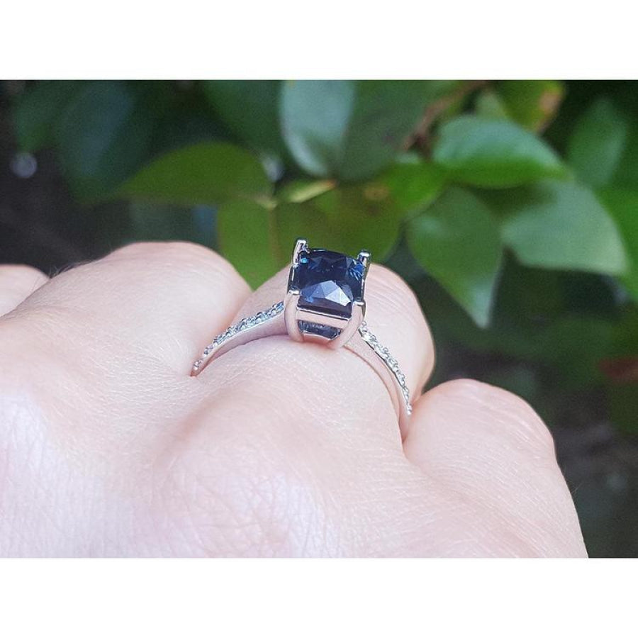 18K white gold ring with a radiant-cut blue sapphire and diamond accents on a hand.