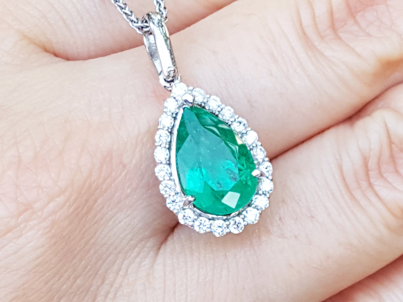 Teardrop-shaped emerald pendant on a white gold chain held between fingers.