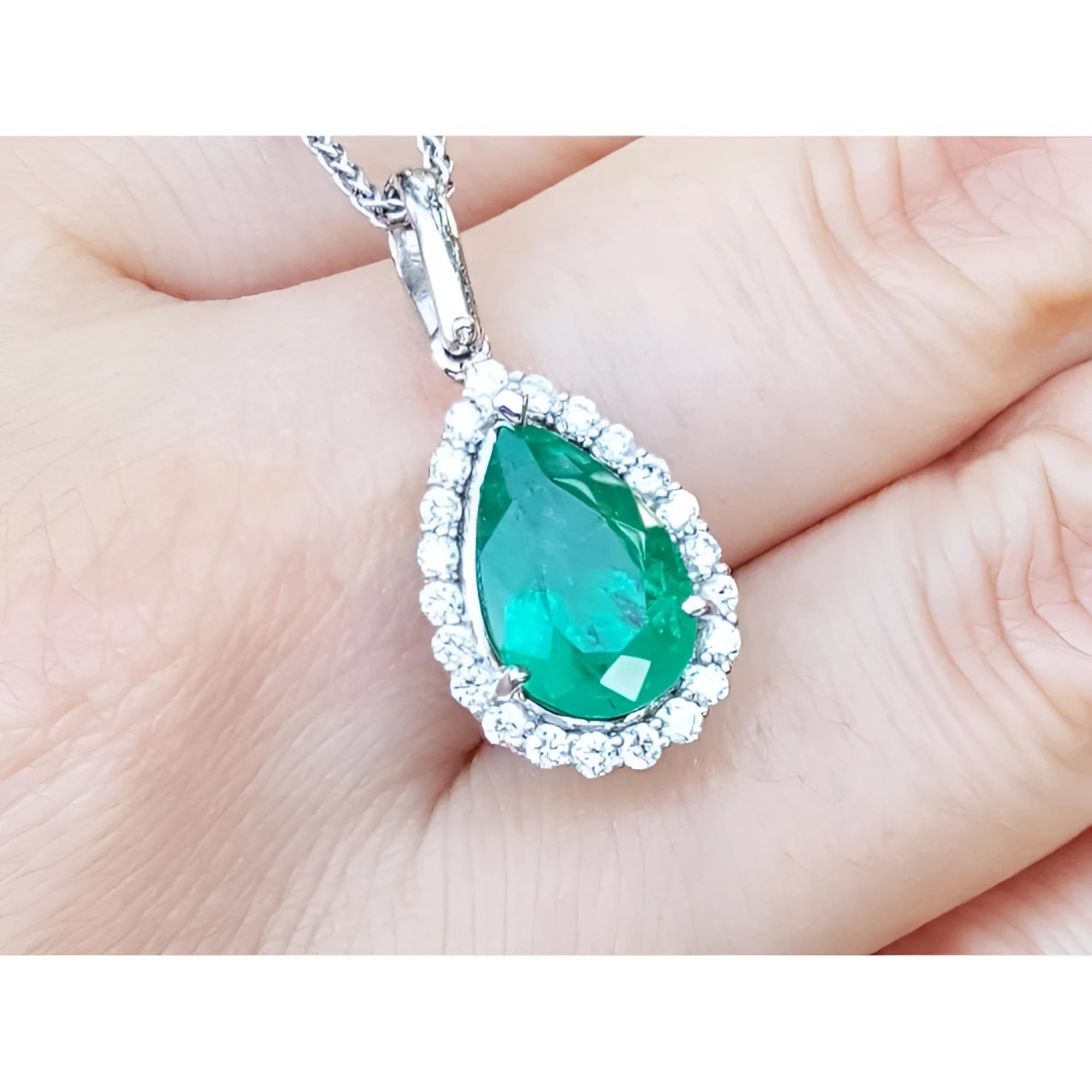 Pear-shaped deep green emerald pendant with diamond halo, set in 18K white gold.