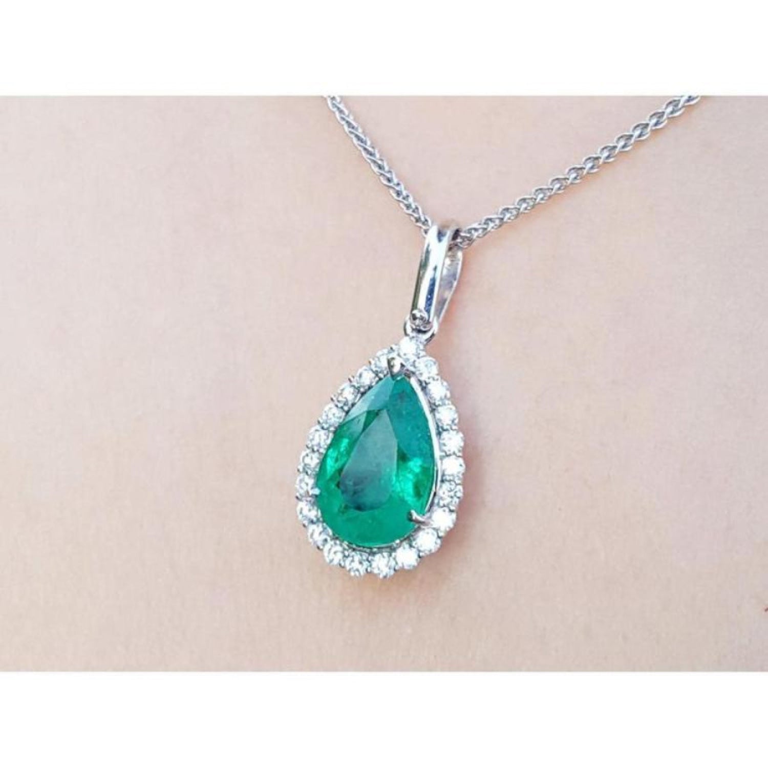 Emerald teardrop pendant with natura halo diamond accents on a beige skin background