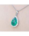 Emerald teardrop pendant with natura halo diamond accents on a beige skin background