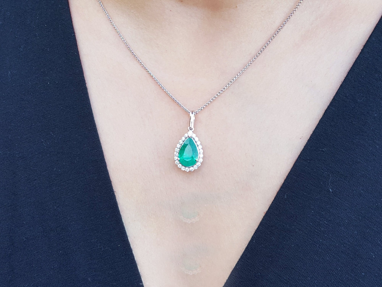 Emerald teardrop pendant on a white gold chain against a dark blue background