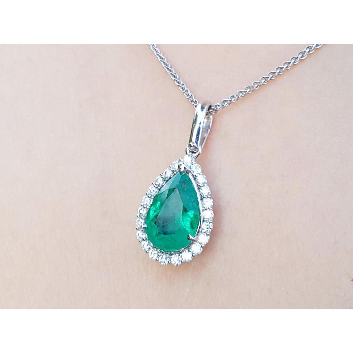 Emerald teardrop pendant with diamond accents on a beige skin background