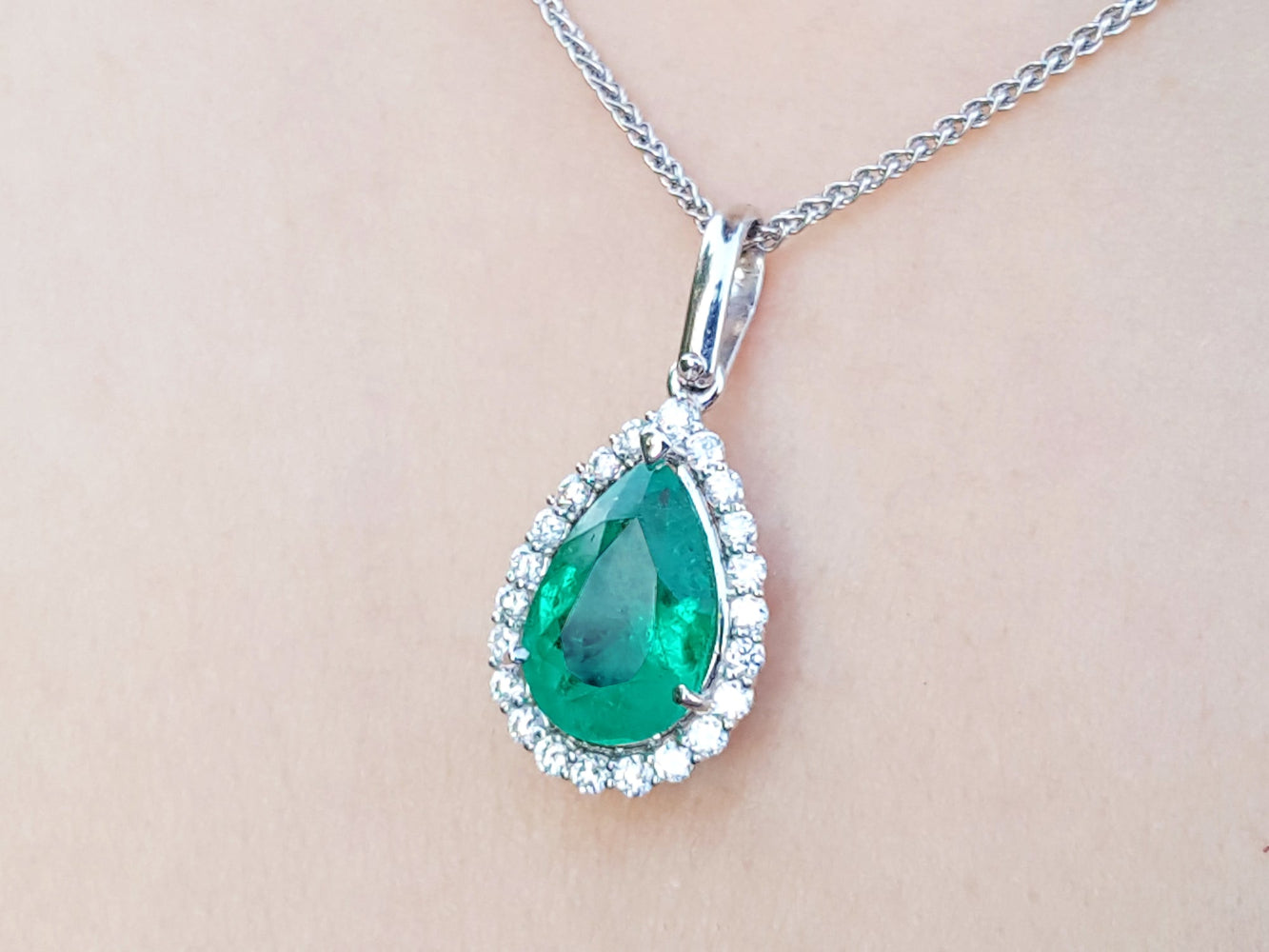 Emerald teardrop pendant with diamond accents on a beige skin background