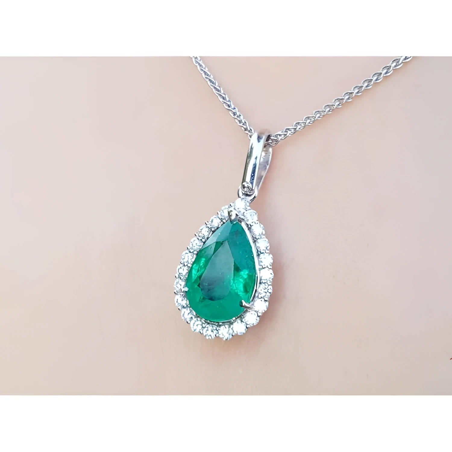 Emerald teardrop pendant with diamond accents on a beige skin background