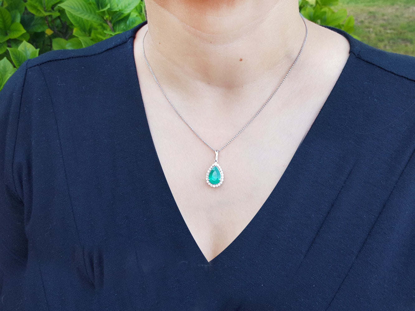A woman wearing a necklace with a natural colombian emerald pendant against a natural background