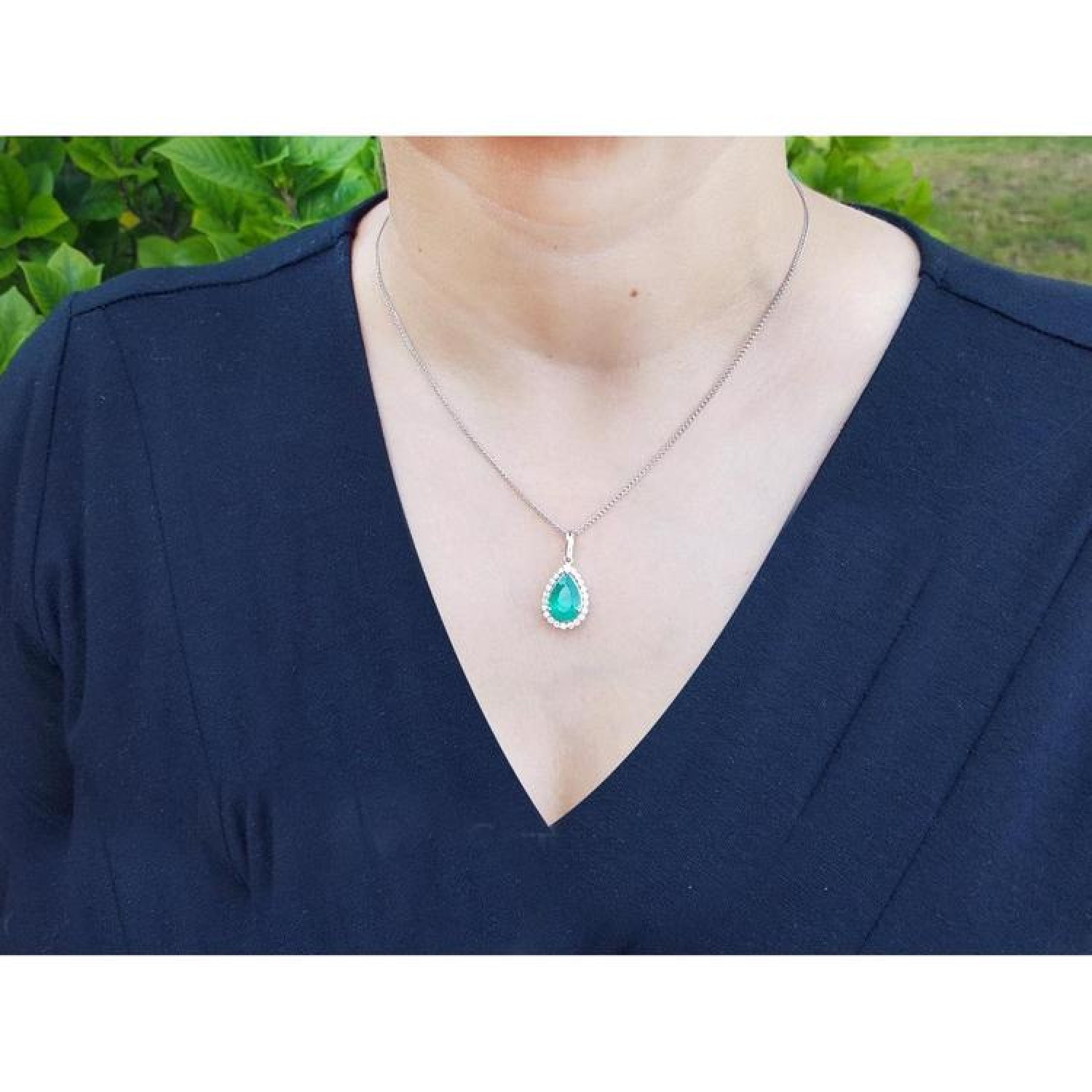 18K white gold pear-shaped emerald pendant with diamond halo on a woman's neck.