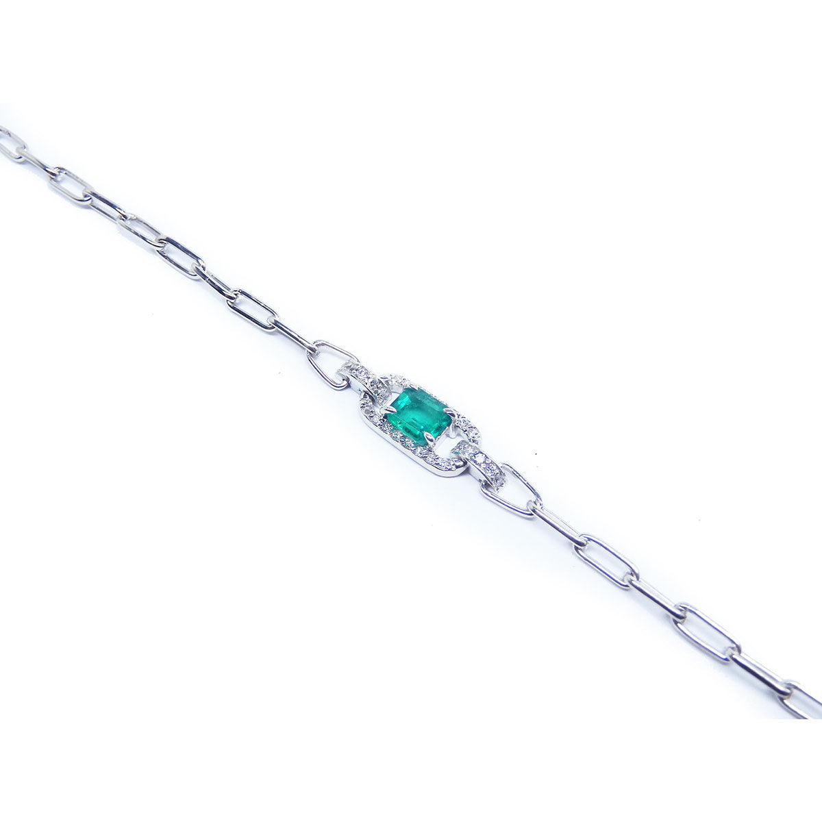 A white gold paperclip bracelet with a colombian emerald on a top far view.