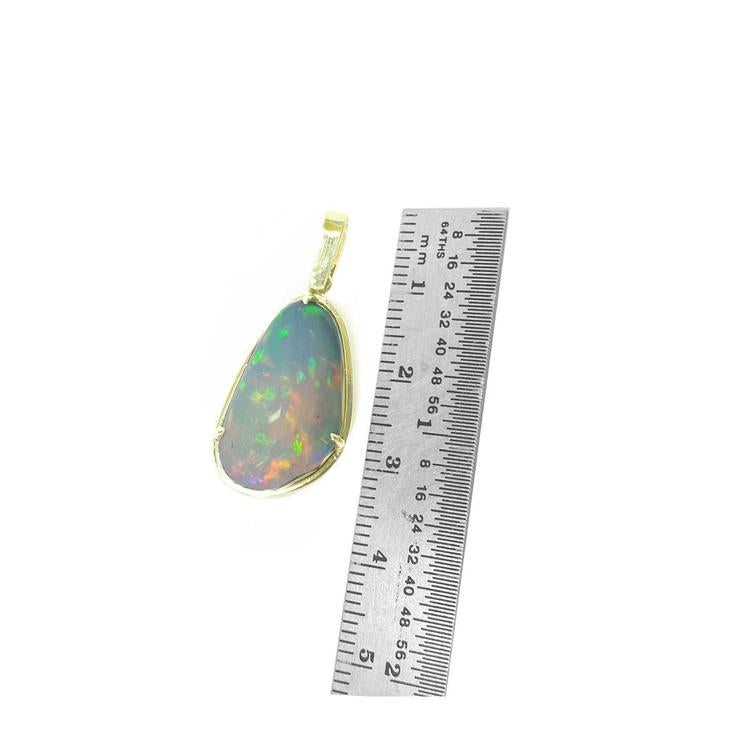 Natural Ethiopian opal pendant with rainbow flashes, set in 14K yellow gold, next to a ruler.
