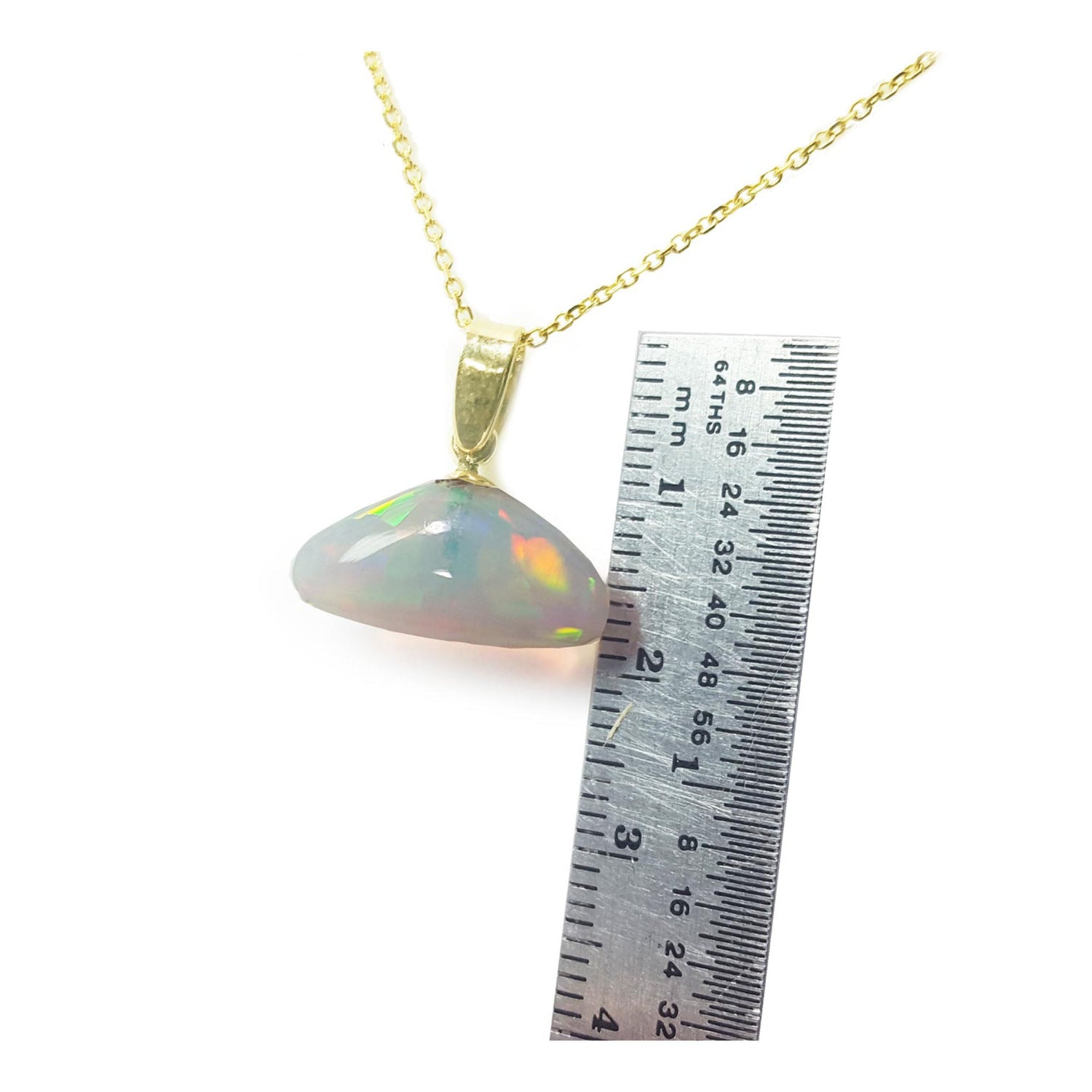 Opal pendant on a gold chain with a ruler for scale on a white background
