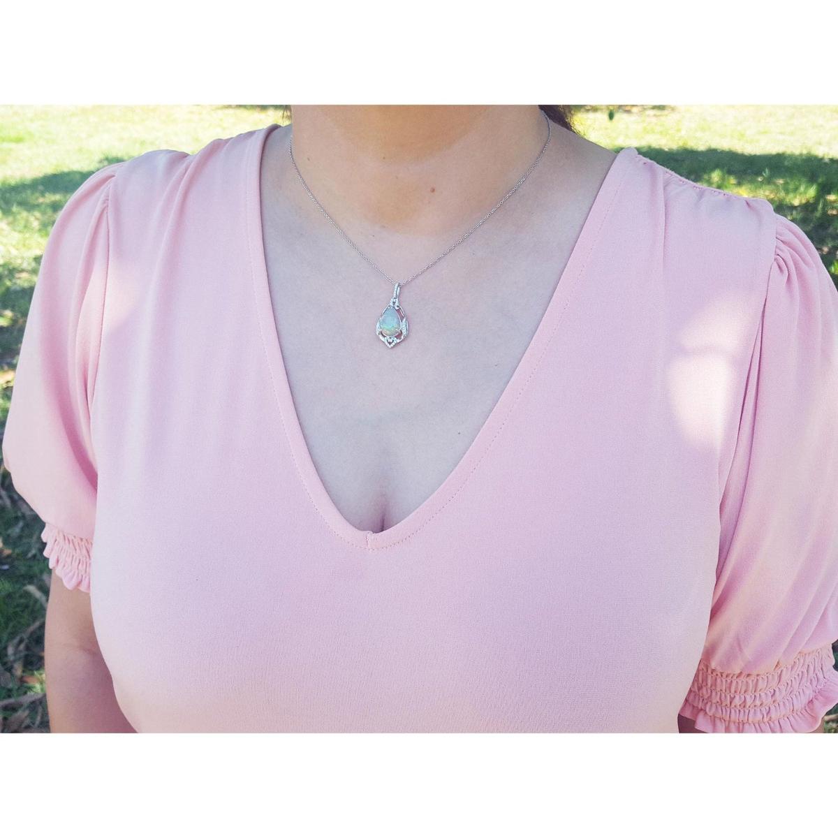 Person wearing a light pink top with an opal pendant necklace outdoors.