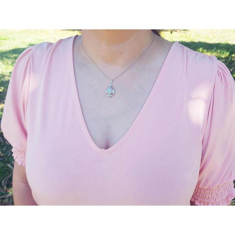 Pear-shaped Welo Ethiopian opal pendant in sterling silver with cubic zirconia, worn on a pink top.