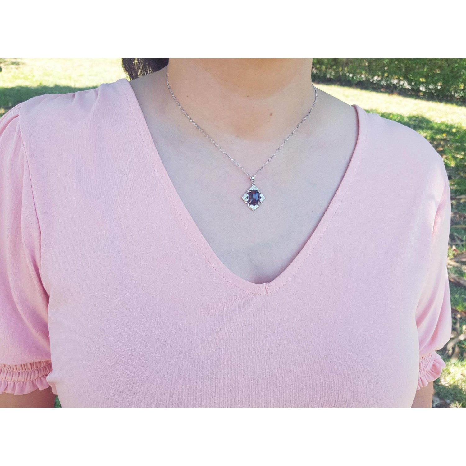 A woman wearing a pink blouse with a necklace featuring a black opal pendant outdoors.