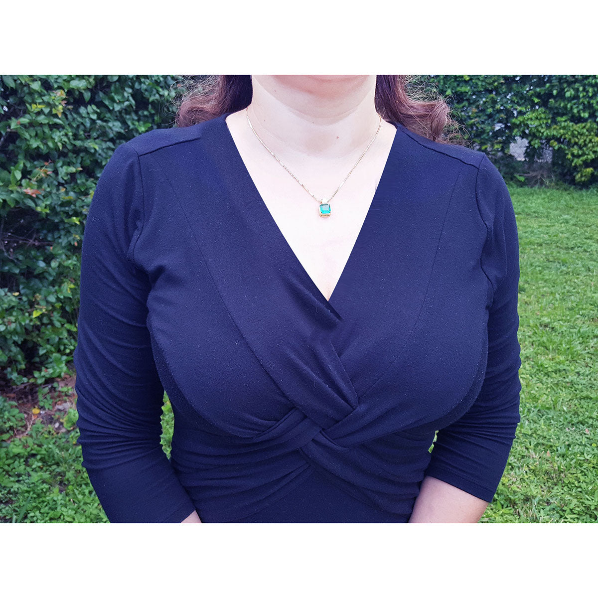 Woman wearing a navy blue dress and an Asscher cut emerald necklace pendant with a blurred green background