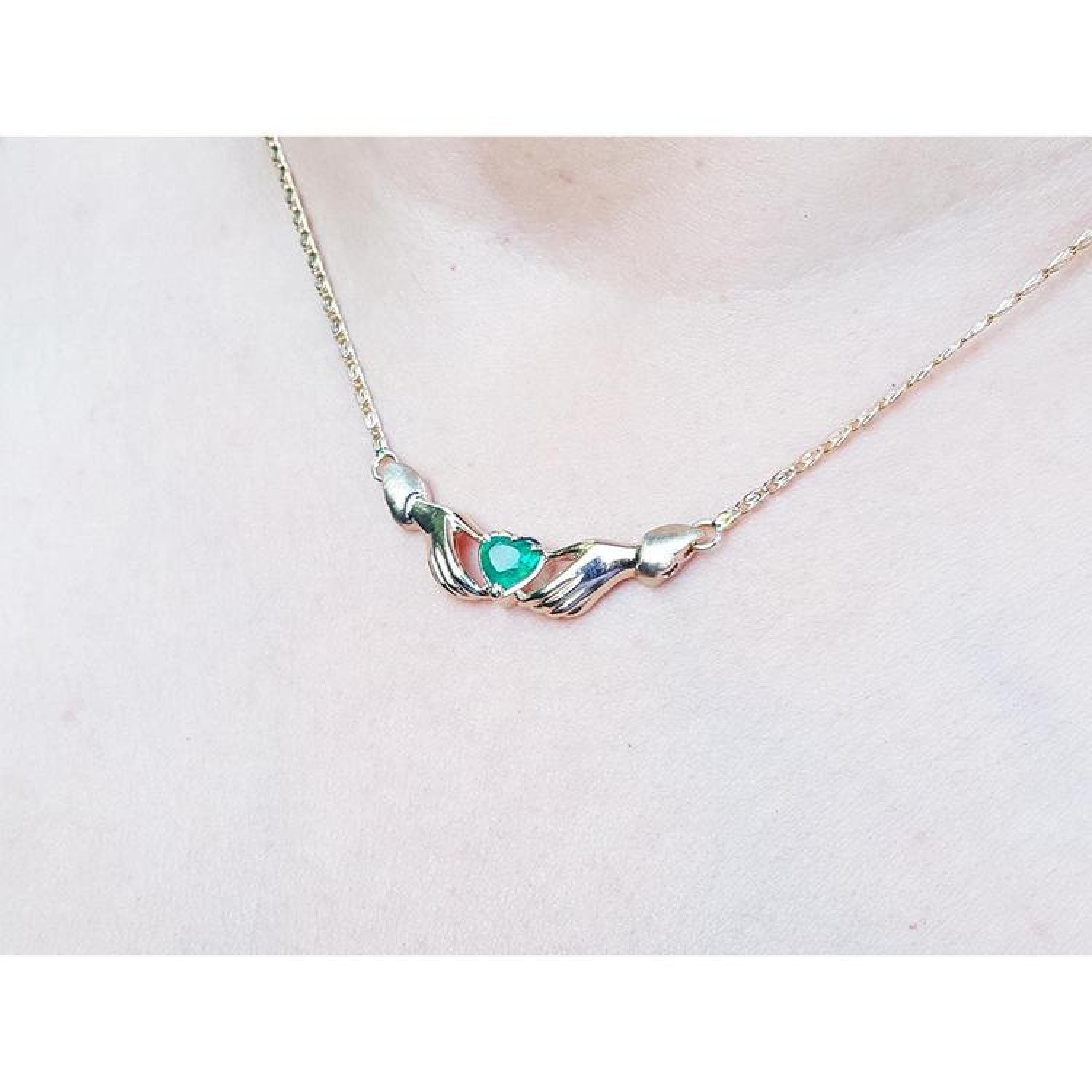 14K yellow gold Claddagh necklace with a heart-cut emerald, worn on a chest.