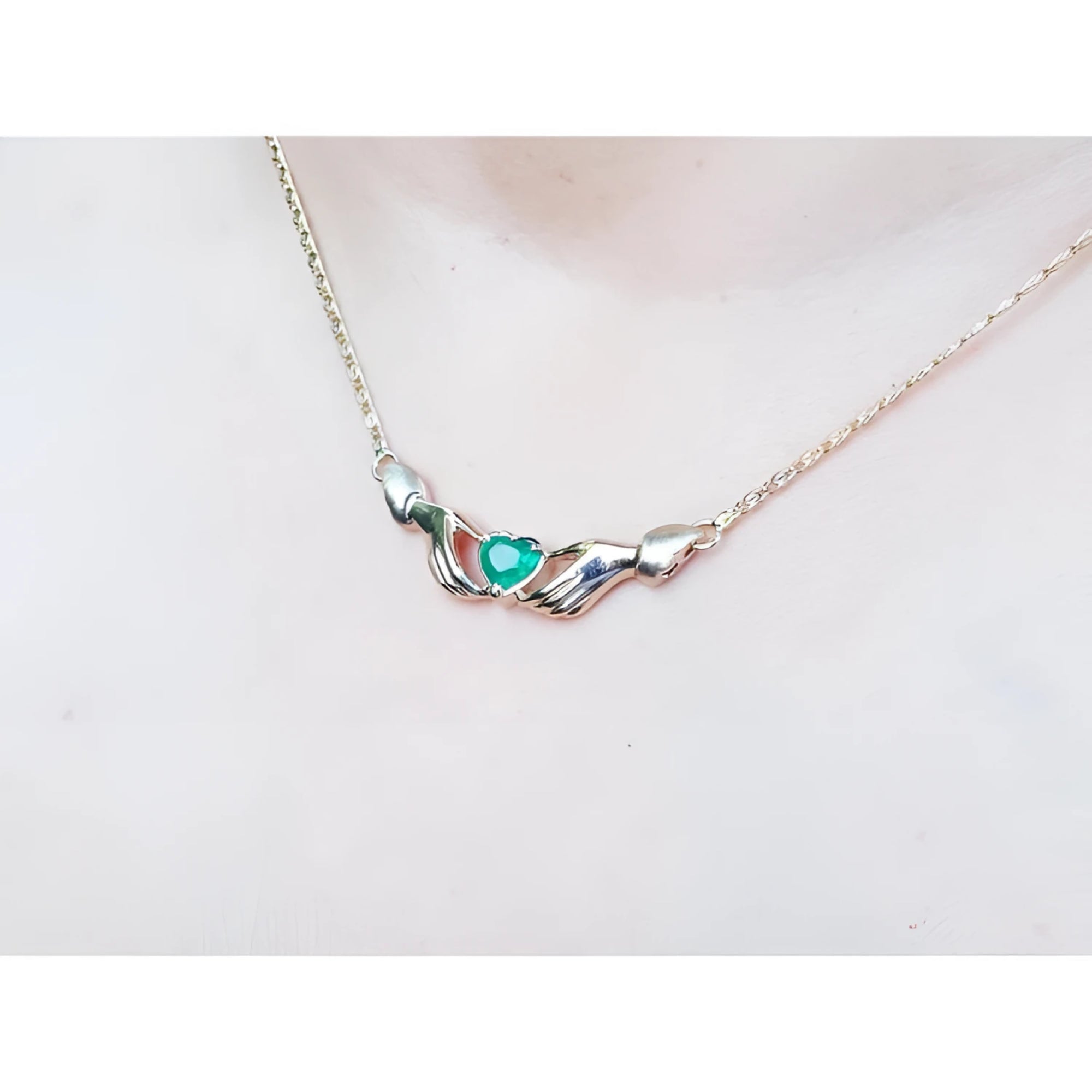 14K yellow gold Claddagh necklace with a heart-cut emerald, worn on a chest.