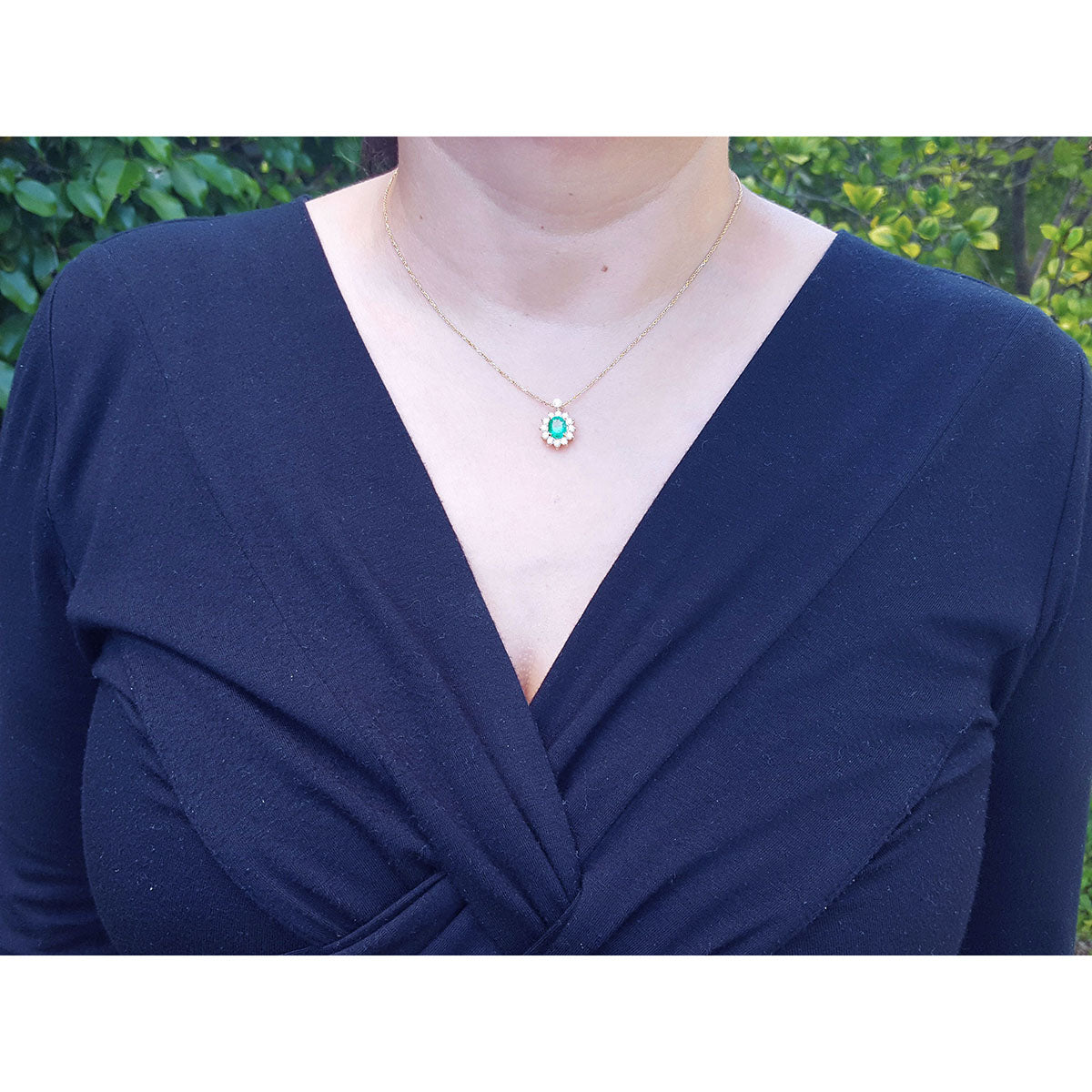 Navy blue top worn by a woman with an emerald necklace against a blurred green leafy background