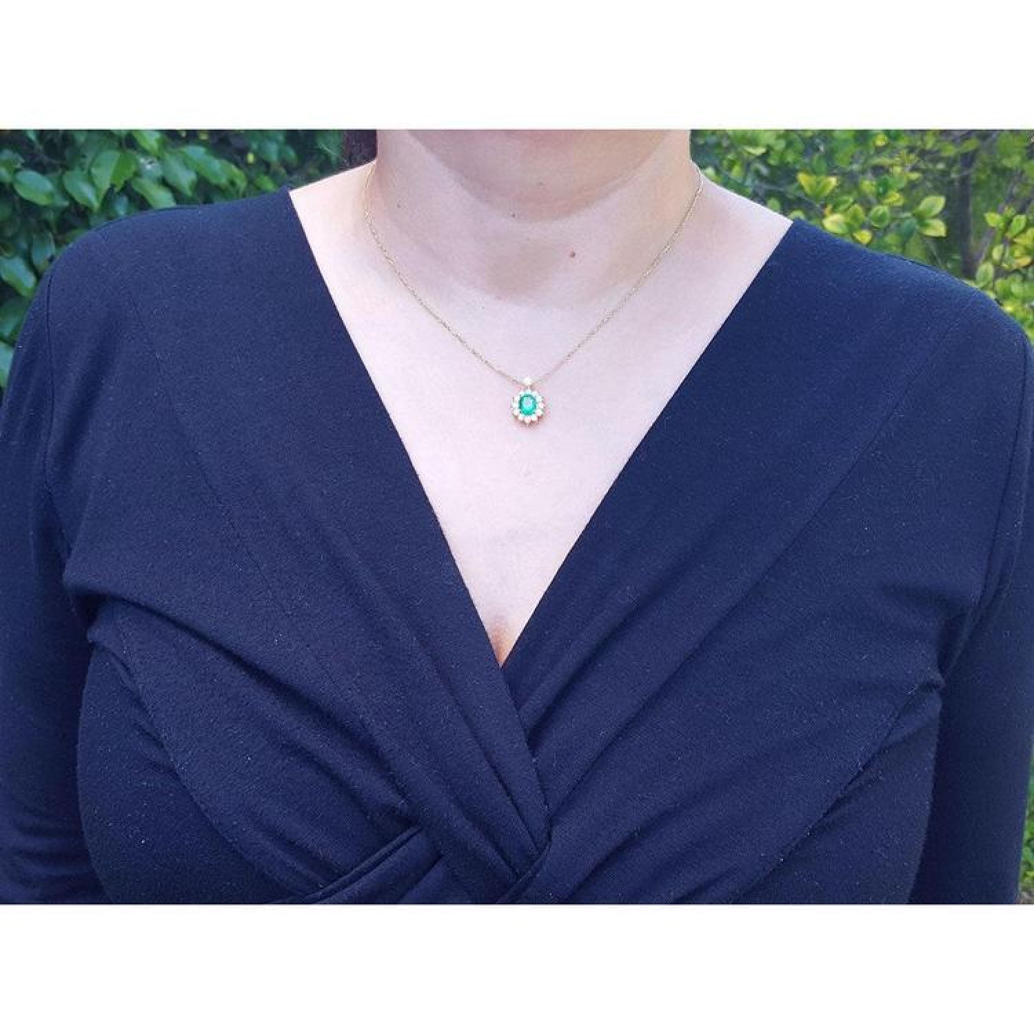 Oval cut emerald and natural diamond pendant necklace on a 14K yellow gold chain, worn on a model.