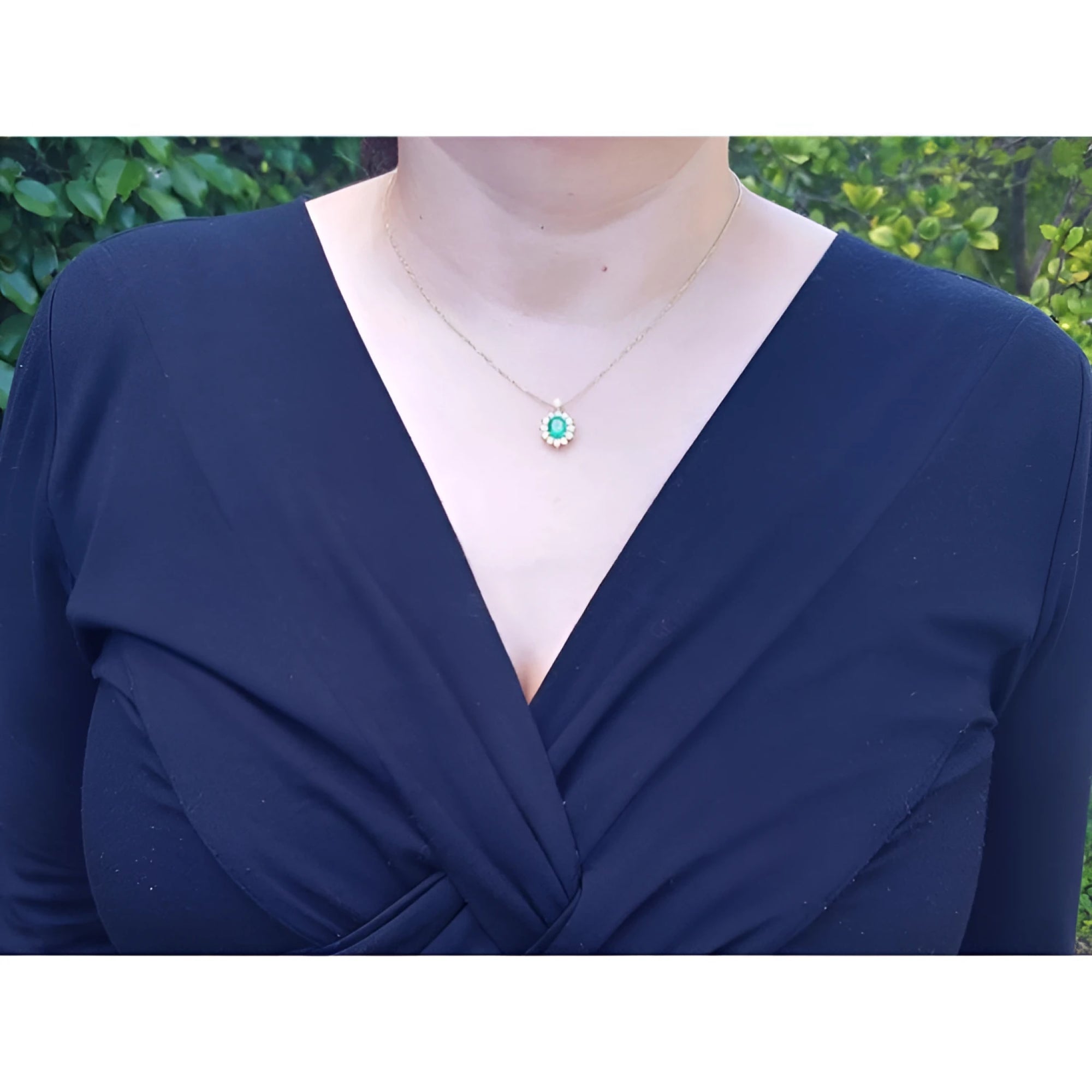 Oval cut emerald and natural diamond pendant necklace on a 14K yellow gold chain, worn on a model.