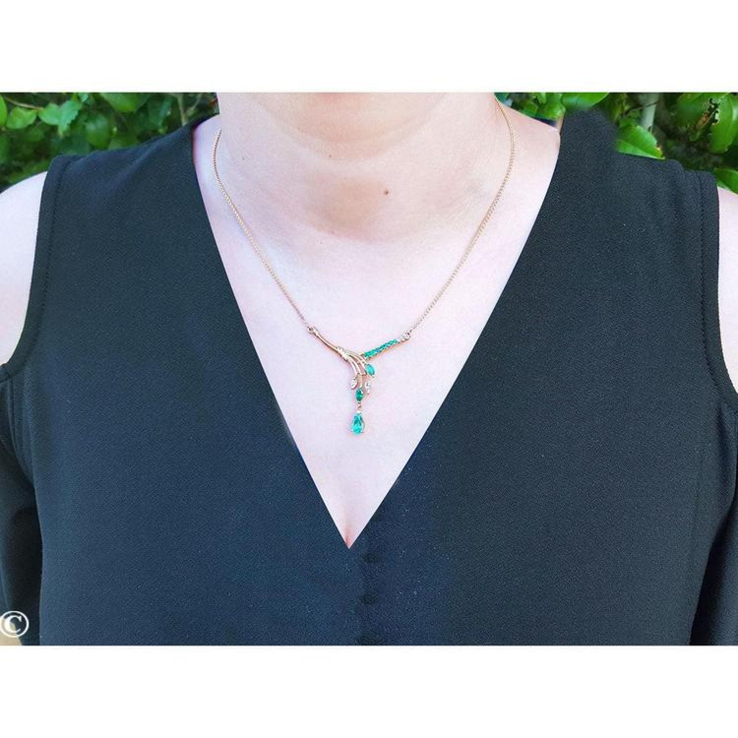 14K yellow gold necklace with marquise and pear-shaped Colombian emeralds and diamonds on a woman's neck.